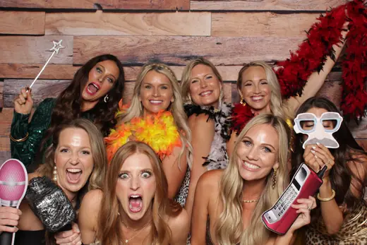 Family group in party hats and novelty glasses crowded into one frame against a gold sequin backdrop